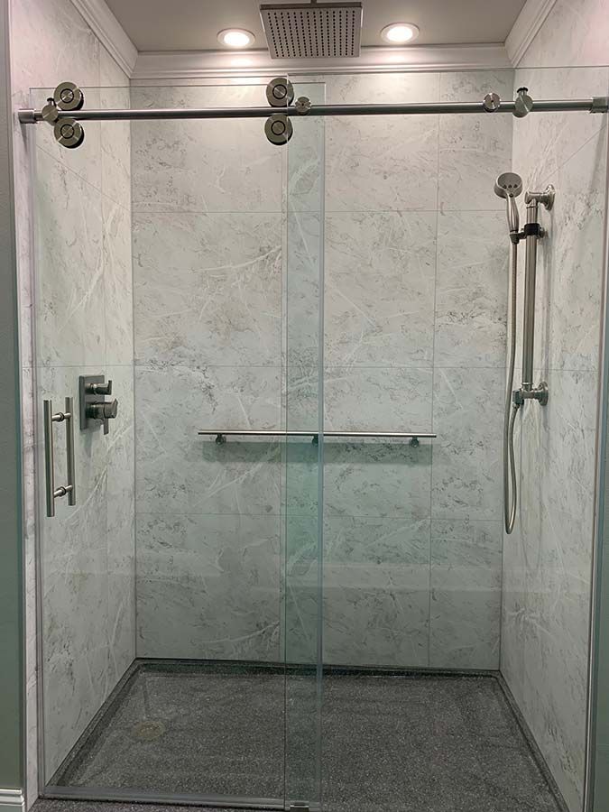 Low curb shower pan in a safer bathroom renovation with white marble laminate shower wall panels - The Bath Doctor 