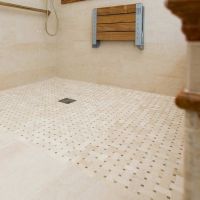 Roll in wheelchair accessible shower with a mosaic tile floor and a fold down seat - Innovate Building Solutions 