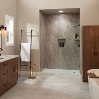Elegant bathroom featuring Emperado Light slab-look shower wall panels, rich walnut cabinetry, matte black fixtures, light gray flooring, a frameless glass shower enclosure, and a freestanding soaking tub.