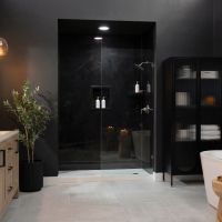 Luxury bathroom featuring Nero Marquina slab-look shower wall panels, dark charcoal walls, a frameless glass shower enclosure, warm wood vanity cabinetry, matte black fixtures, gray floor tile, and a freestanding soaking tub.