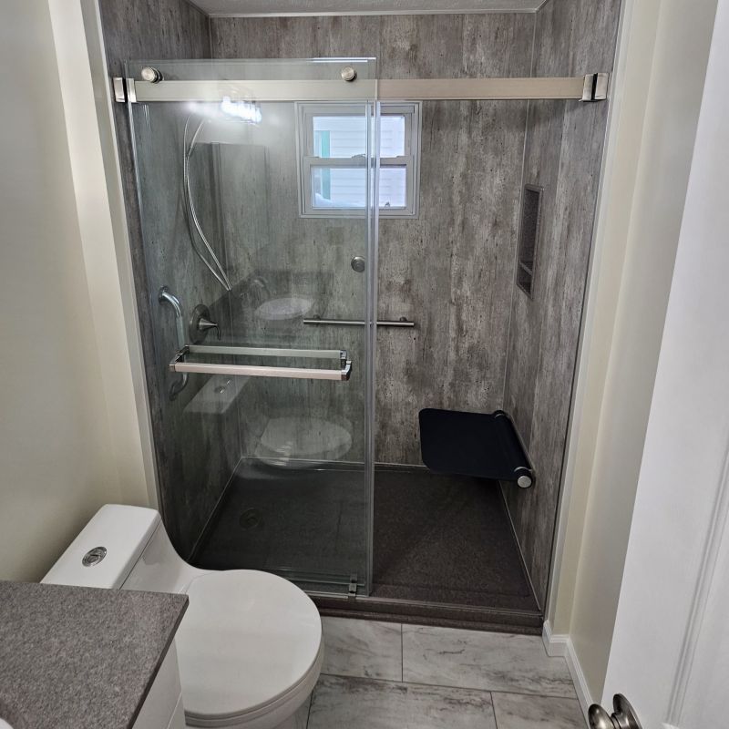 Cleveland Ohio tub-to-shower conversion with walk-in shower, Cracked Cement wall panels, sliding glass door, fold-down seat, grab bars, and low-threshold shower base.