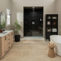 Modern luxury bathroom featuring Nero Marquina slab-look shower wall panels, a frameless glass shower enclosure, light wood vanity cabinets, beige walls, matte black fixtures, large-format tile flooring, and a freestanding soaking tub.