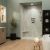 Contemporary bathroom featuring Crema Marfil marble-look shower wall panels, sage green walls, a light oak vanity, matte black fixtures, light wood flooring, and a freestanding soaking tub beside a spacious walk-in shower.
