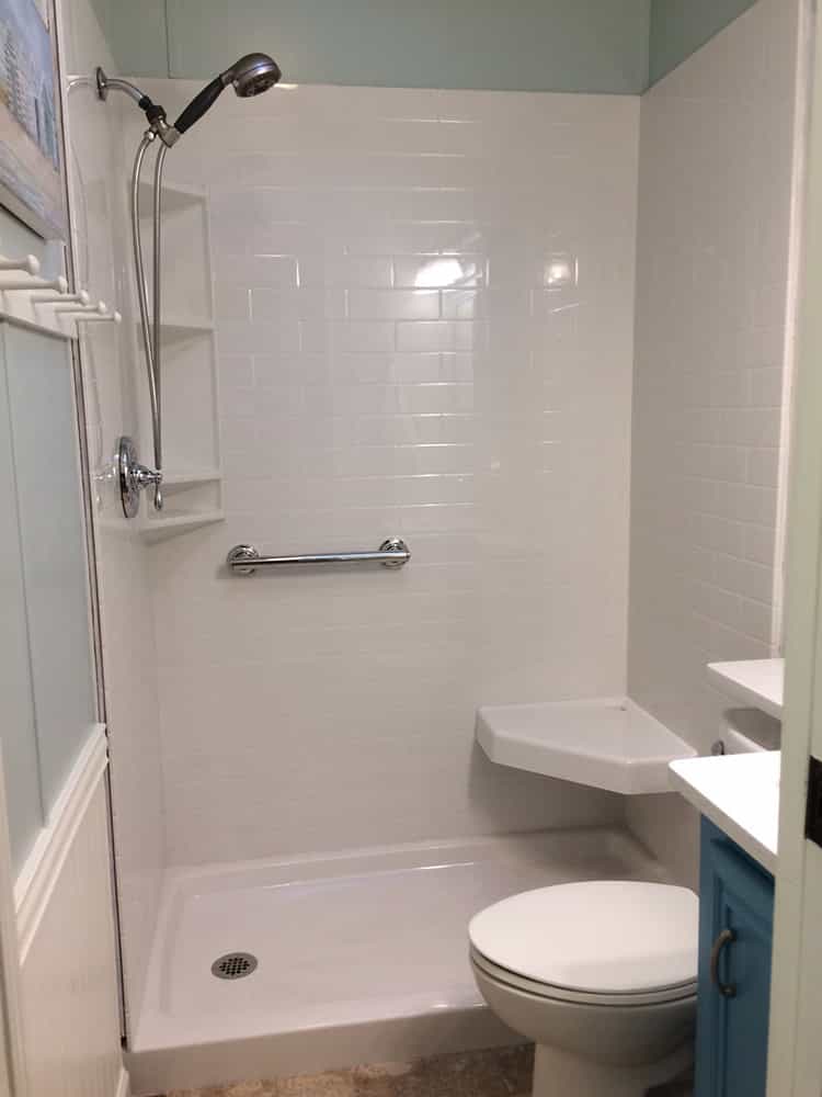 White grout free subway tile wall panels with an angled corner seat and triple shower caddy 